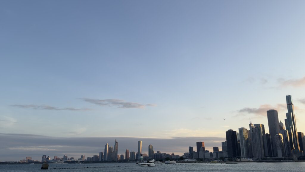 Chicago skyline at dusk viewed from Navy Pier, with Lake Michigan in the foreground, boats on the water, and the city’s high-rise buildings glowing in the evening light.
