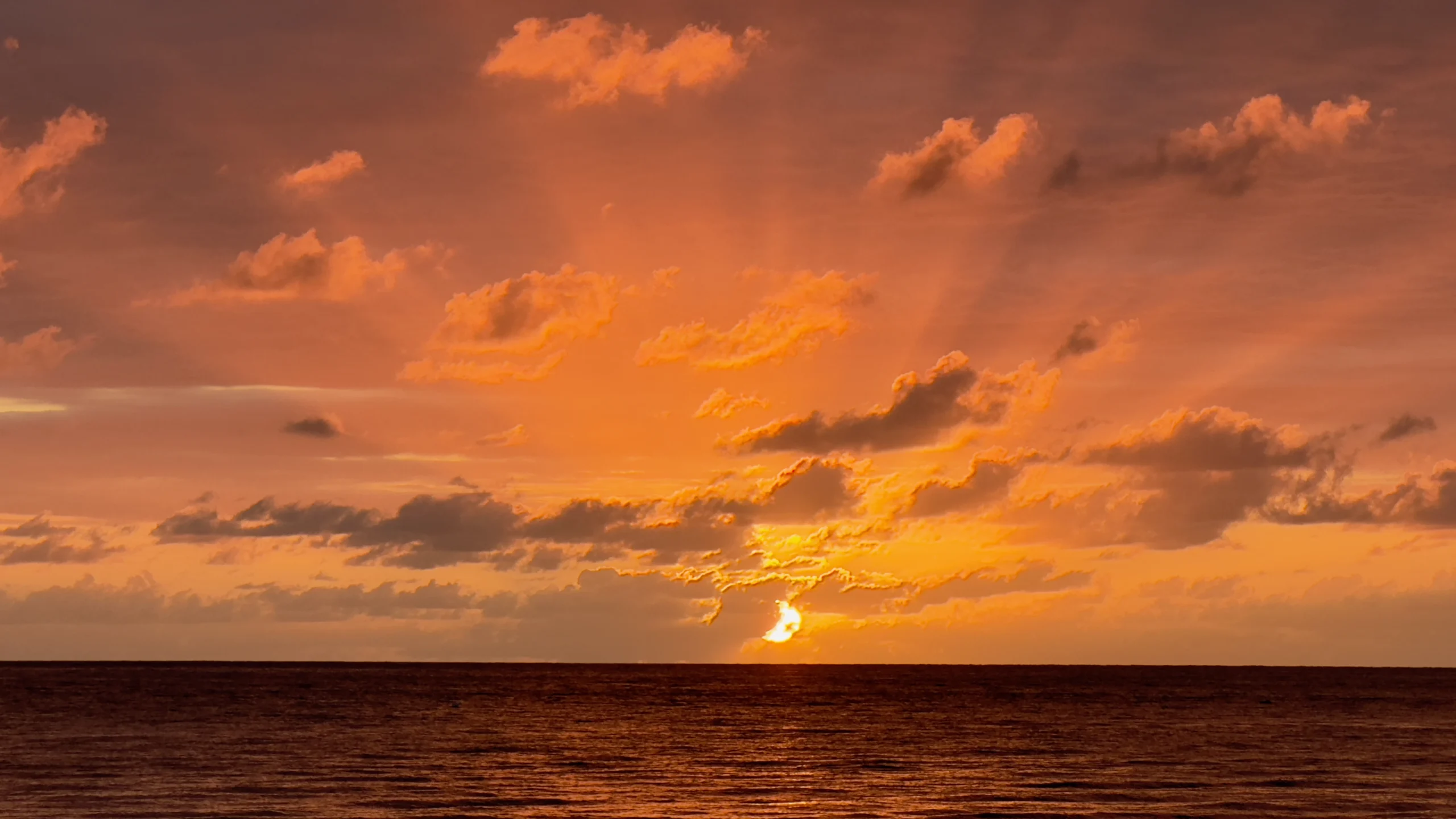 Golden sunset over the Caribbean Sea in Negril, Jamaica, with orange clouds reflecting across calm ocean waters.